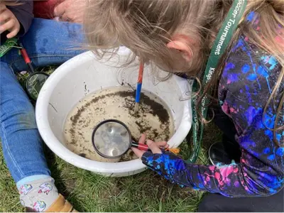 Children with a magnifying glass looking in pail