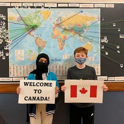 Student holding a piece of paper that reads Welcome To Canada and another student holding a picture of the Canadian Flag