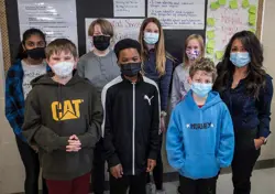 Picture of teacher with students in front of a board of completed work